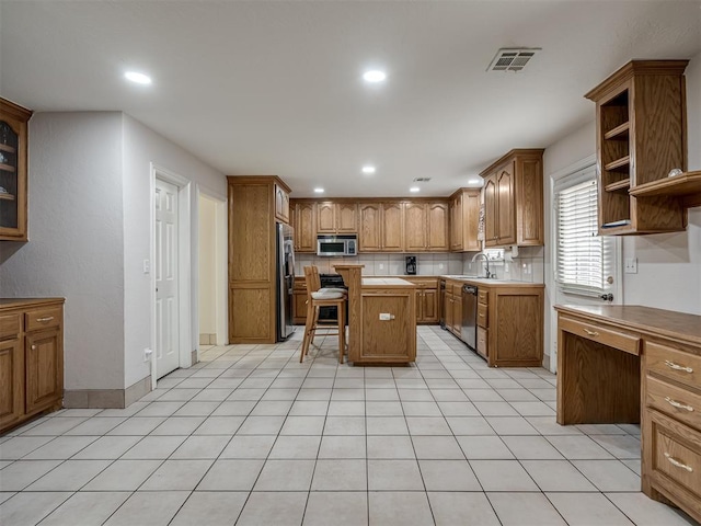 kitchen featuring a breakfast bar area, brown cabinetry, visible vents, decorative backsplash, and appliances with stainless steel finishes