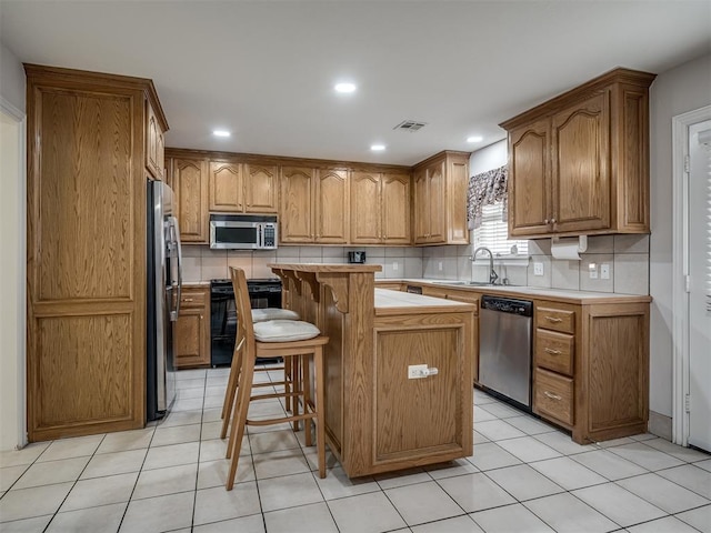 kitchen featuring a sink, a kitchen island, stainless steel appliances, light countertops, and decorative backsplash