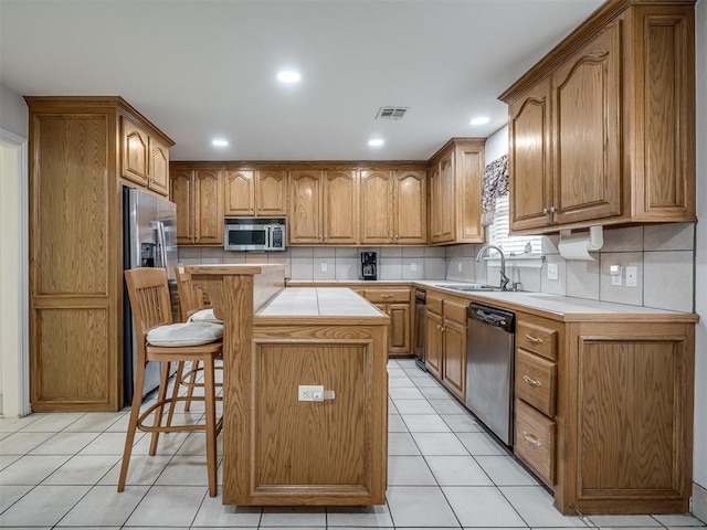 kitchen with light tile patterned floors, a kitchen island, a sink, stainless steel appliances, and light countertops