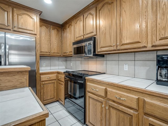 kitchen with tasteful backsplash, tile counters, light tile patterned floors, brown cabinets, and stainless steel appliances