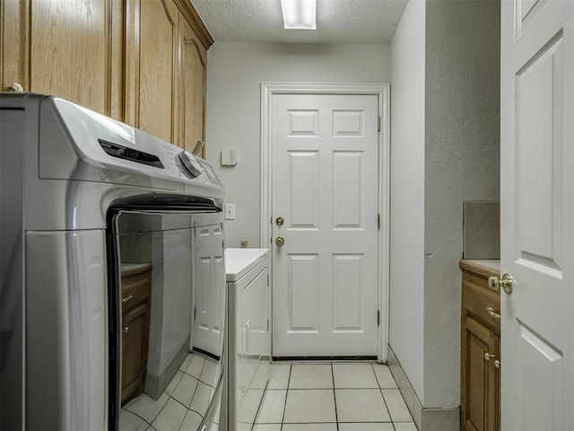 clothes washing area with light tile patterned floors, washing machine and clothes dryer, cabinet space, a textured ceiling, and a textured wall