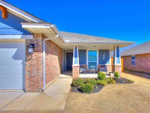 property entrance featuring brick siding, an attached garage, a porch, and roof with shingles