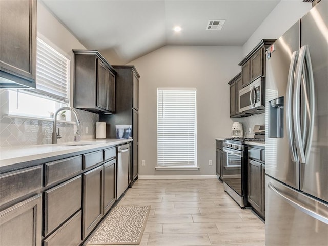 kitchen with backsplash, dark brown cabinetry, light countertops, lofted ceiling, and appliances with stainless steel finishes