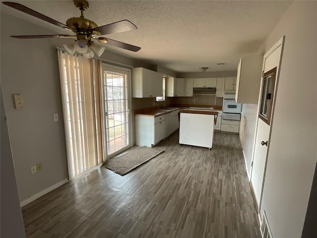 kitchen with a kitchen island, dark wood finished floors, a textured ceiling, white cabinetry, and white oven