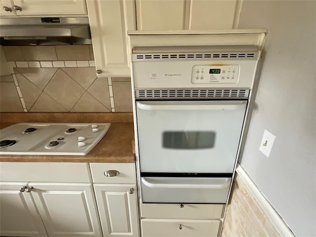 kitchen featuring tasteful backsplash, under cabinet range hood, white cabinets, white appliances, and a warming drawer