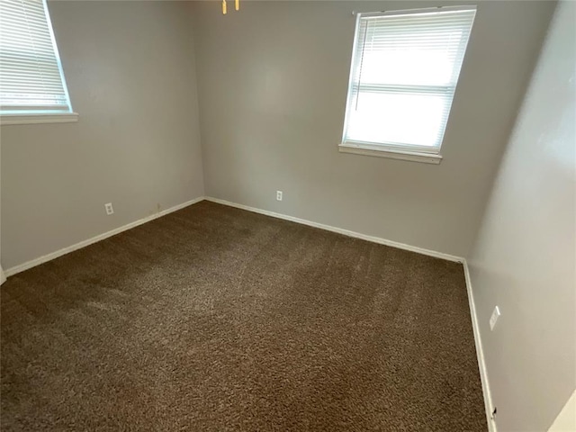 spare room with baseboards and dark carpet