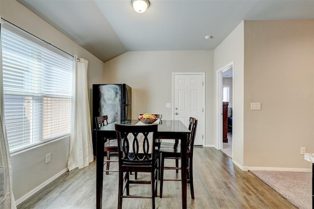 dining area featuring baseboards, lofted ceiling, and light wood-style floors