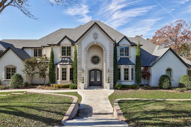 french provincial home featuring stucco siding, french doors, a shingled roof, and a front lawn