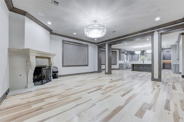 basement featuring visible vents, a fireplace, ornamental molding, light wood-type flooring, and a chandelier