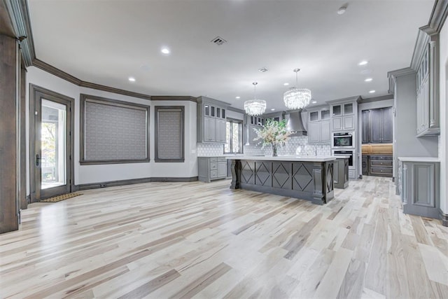 kitchen with visible vents, gray cabinetry, light countertops, wall chimney range hood, and a chandelier