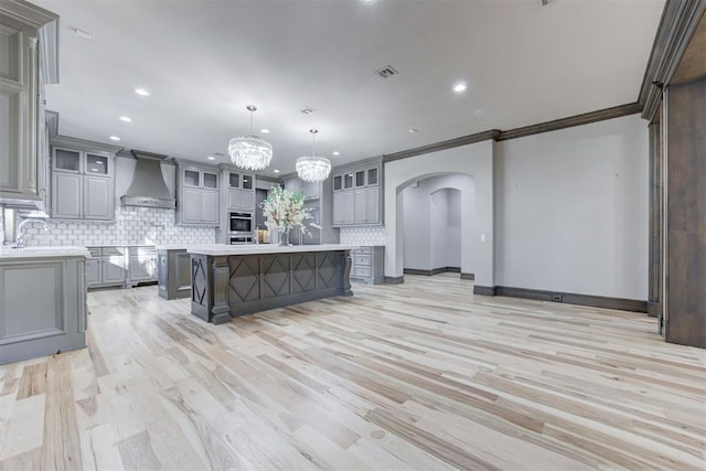 kitchen featuring premium range hood, arched walkways, gray cabinetry, decorative backsplash, and light countertops