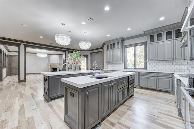 kitchen with visible vents, an island with sink, gray cabinets, ornamental molding, and a sink