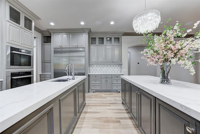 kitchen featuring a sink, decorative backsplash, gray cabinetry, glass insert cabinets, and built in fridge