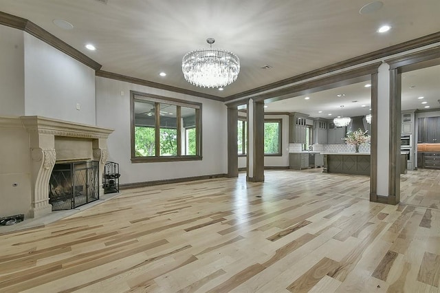 2747 Walking Woods Trl, Edmond, OK 73049 - unfurnished living room with ornate columns, ornamental molding, a chandelier, a fireplace, and light wood-style floors