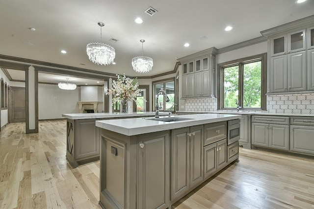 2747 Walking Woods Trl, Edmond, OK 73049 - kitchen with gray cabinetry, an island with sink, a sink, crown molding, and a chandelier
