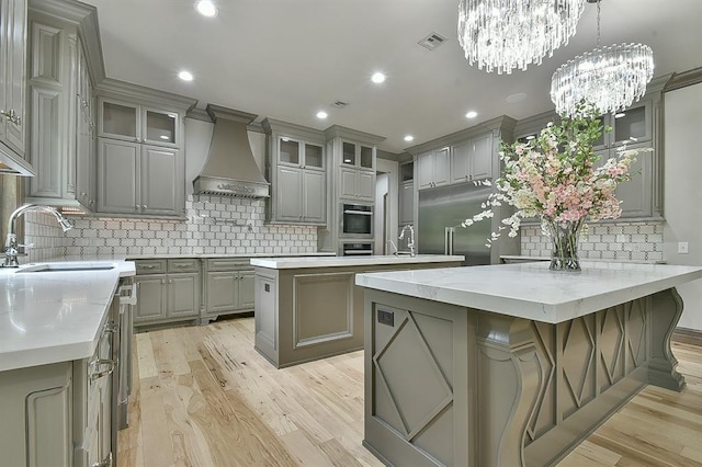 2747 Walking Woods Trl, Edmond, OK 73049 - kitchen featuring gray cabinets, custom range hood, a sink, a kitchen island, and decorative backsplash