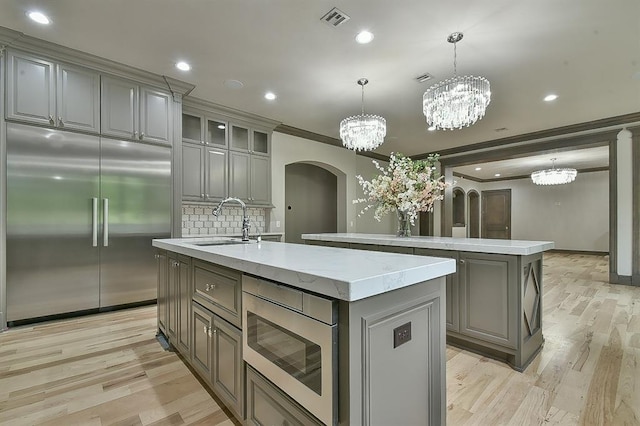 2747 Walking Woods Trl, Edmond, OK 73049 - kitchen featuring built in appliances, a center island with sink, gray cabinetry, arched walkways, and ornamental molding