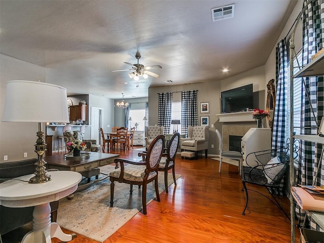 dining room with wood finished floors, visible vents, baseboards, a fireplace, and ceiling fan with notable chandelier