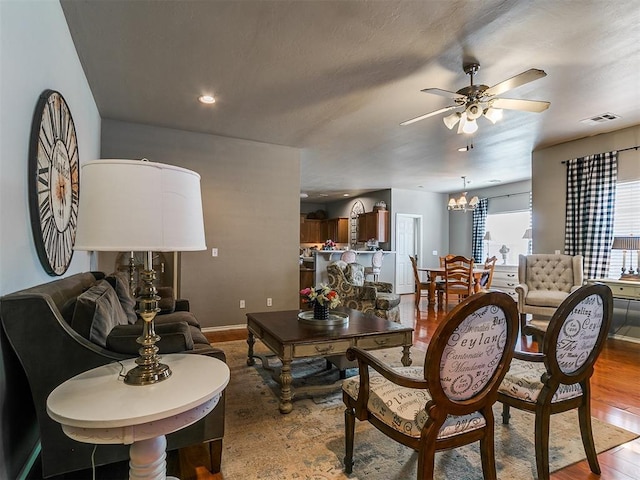 living room with visible vents, ceiling fan with notable chandelier, wood finished floors, recessed lighting, and baseboards