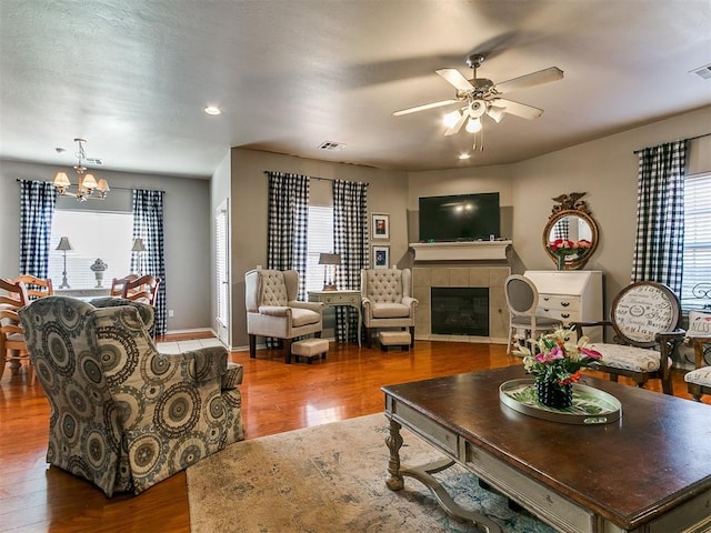 living area with visible vents, baseboards, a tiled fireplace, ceiling fan with notable chandelier, and wood finished floors