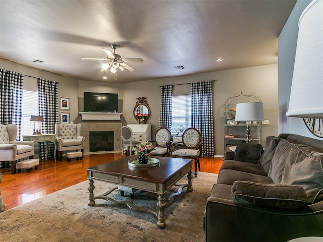 living area featuring ceiling fan, visible vents, wood finished floors, and a tile fireplace