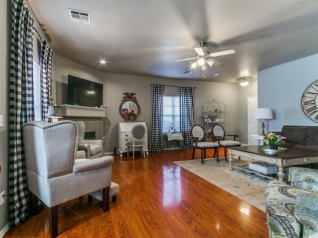 living area featuring visible vents, a fireplace, ceiling fan, and wood finished floors