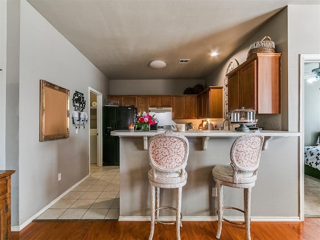 kitchen with visible vents, a kitchen breakfast bar, freestanding refrigerator, a peninsula, and light countertops