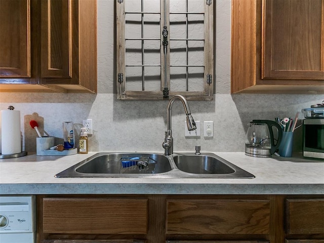 kitchen featuring tasteful backsplash, washer / dryer, light countertops, and a sink