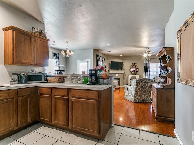 kitchen featuring stainless steel microwave, open floor plan, light countertops, ceiling fan with notable chandelier, and a peninsula