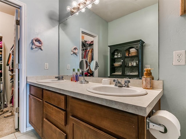 bathroom with tile patterned flooring, a spacious closet, double vanity, and a sink