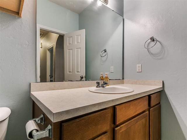 half bath featuring vanity, toilet, and a textured wall