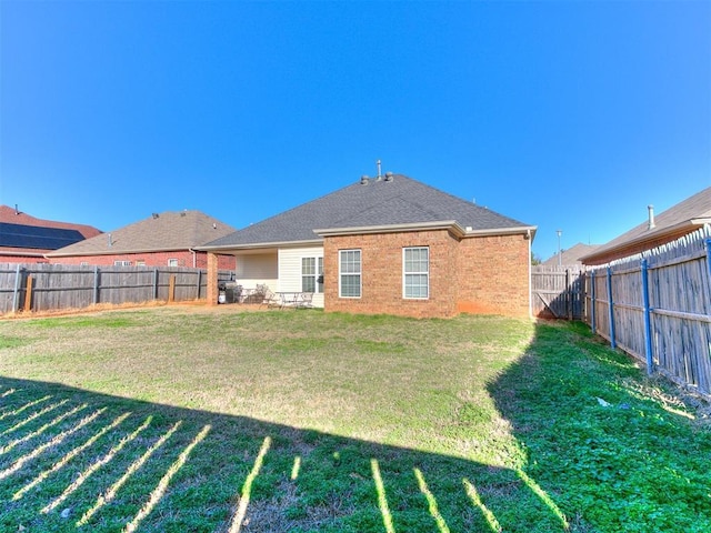 back of house featuring a yard, brick siding, roof with shingles, and a fenced backyard