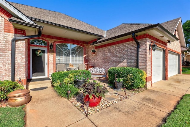 view of exterior entry featuring concrete driveway, a garage, brick siding, and a shingled roof