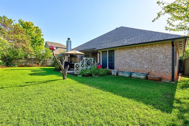 rear view of property with fence, roof with shingles, a chimney, a lawn, and brick siding