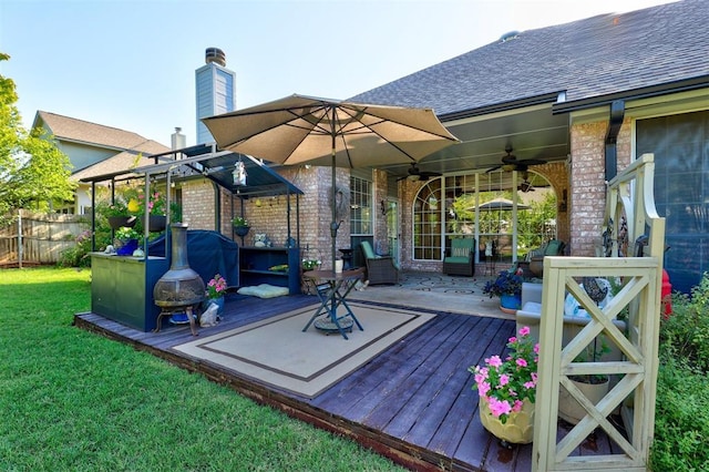 wooden terrace with fence, a ceiling fan, and a lawn