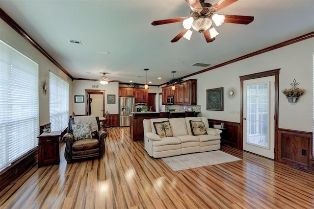 living area featuring visible vents, wainscoting, crown molding, and light wood-type flooring