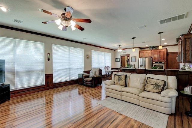 living area featuring visible vents, wood finished floors, a wainscoted wall, and ornamental molding