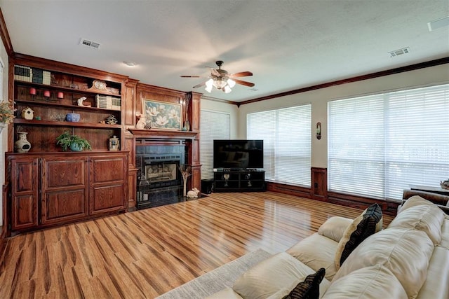 living room featuring a wainscoted wall, crown molding, a fireplace, and visible vents