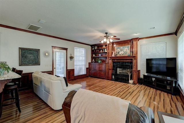 living room featuring wood finished floors, a fireplace, visible vents, and ornamental molding