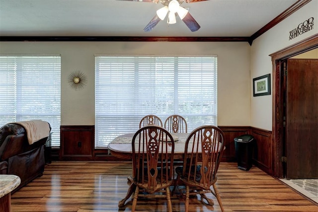 dining room with light wood finished floors, a wainscoted wall, crown molding, and a ceiling fan