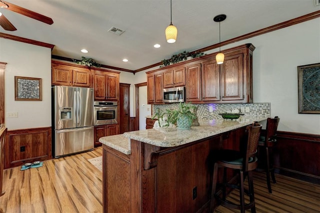 kitchen featuring visible vents, a peninsula, appliances with stainless steel finishes, wainscoting, and crown molding