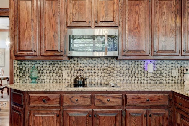 kitchen featuring stainless steel microwave, black electric stovetop, light stone countertops, and backsplash