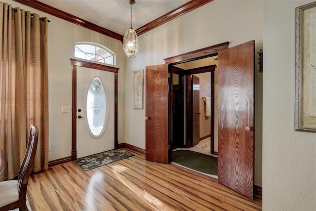 entryway featuring a chandelier, crown molding, baseboards, and wood finished floors