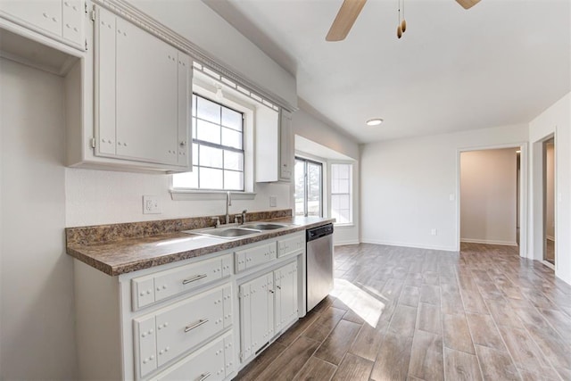 kitchen featuring dark countertops, stainless steel dishwasher, wood finished floors, a ceiling fan, and a sink