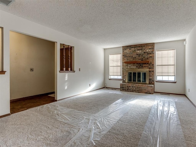 unfurnished living room featuring baseboards, carpet floors, a textured ceiling, and a brick fireplace