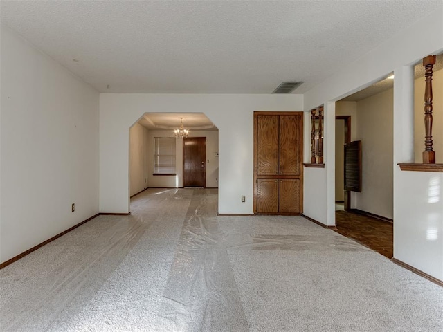 empty room with baseboards, visible vents, arched walkways, a textured ceiling, and light colored carpet