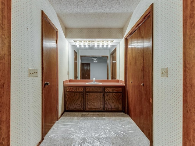 hallway featuring wallpapered walls, a sink, and a textured ceiling