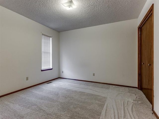 empty room with visible vents, light colored carpet, a textured ceiling, and baseboards