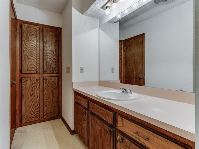 bathroom with a textured ceiling, vanity, and baseboards