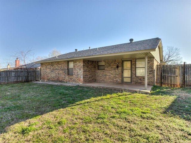 back of property with a lawn, a fenced backyard, brick siding, and a patio area